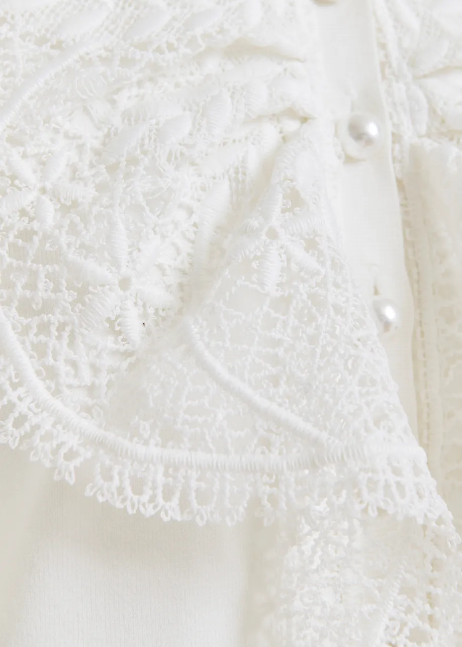 Witte mouwloze polo met kant en parelknopen